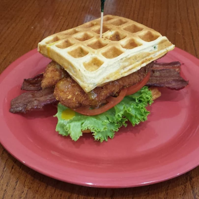 Lola's Chicken Shack's fried chicken and waffle sandwich with bacon, lettuce, and tomato on a red plate.